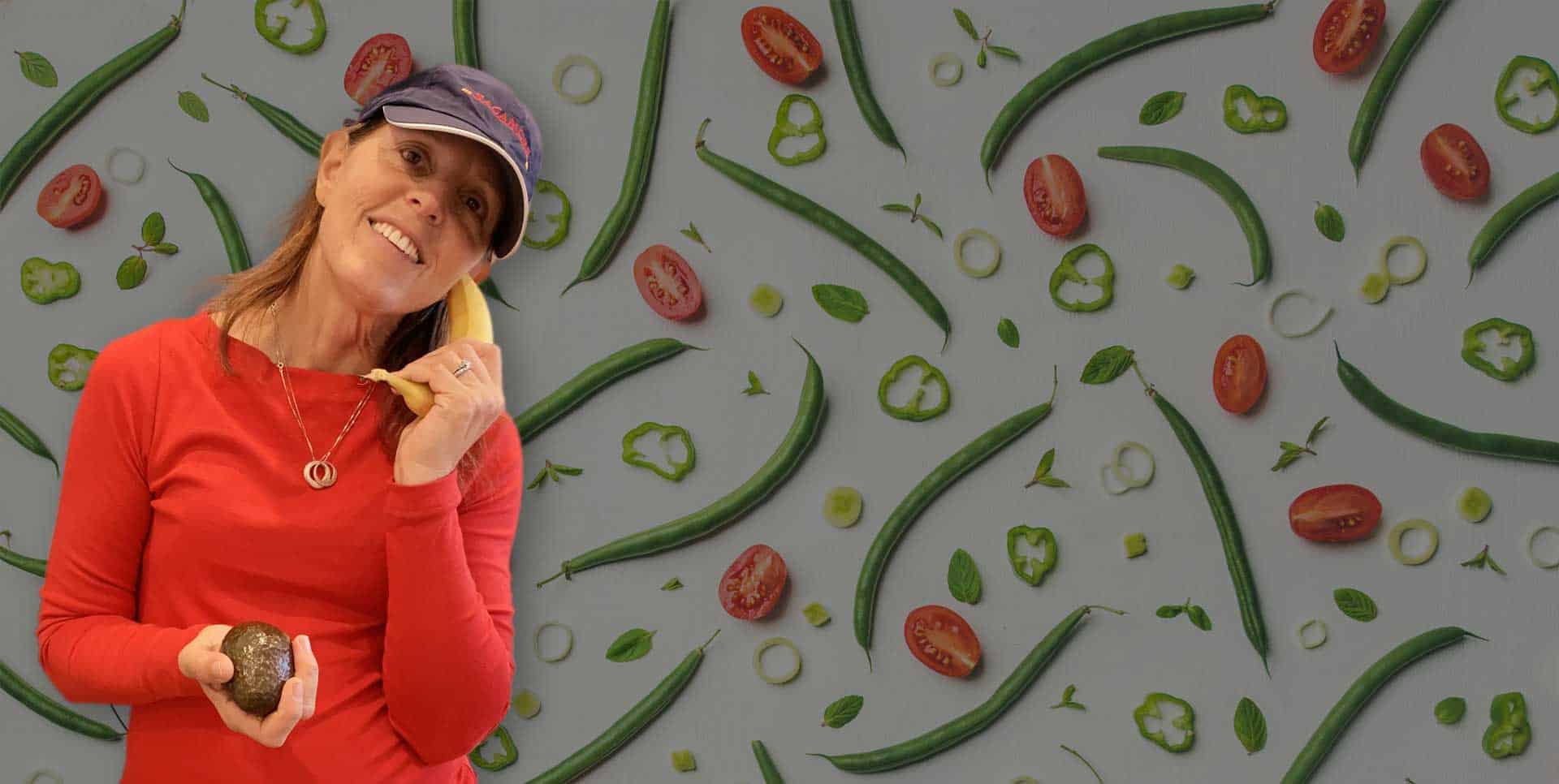 Debbie Sweeney with a banana phone surrounded by fresh vegetables